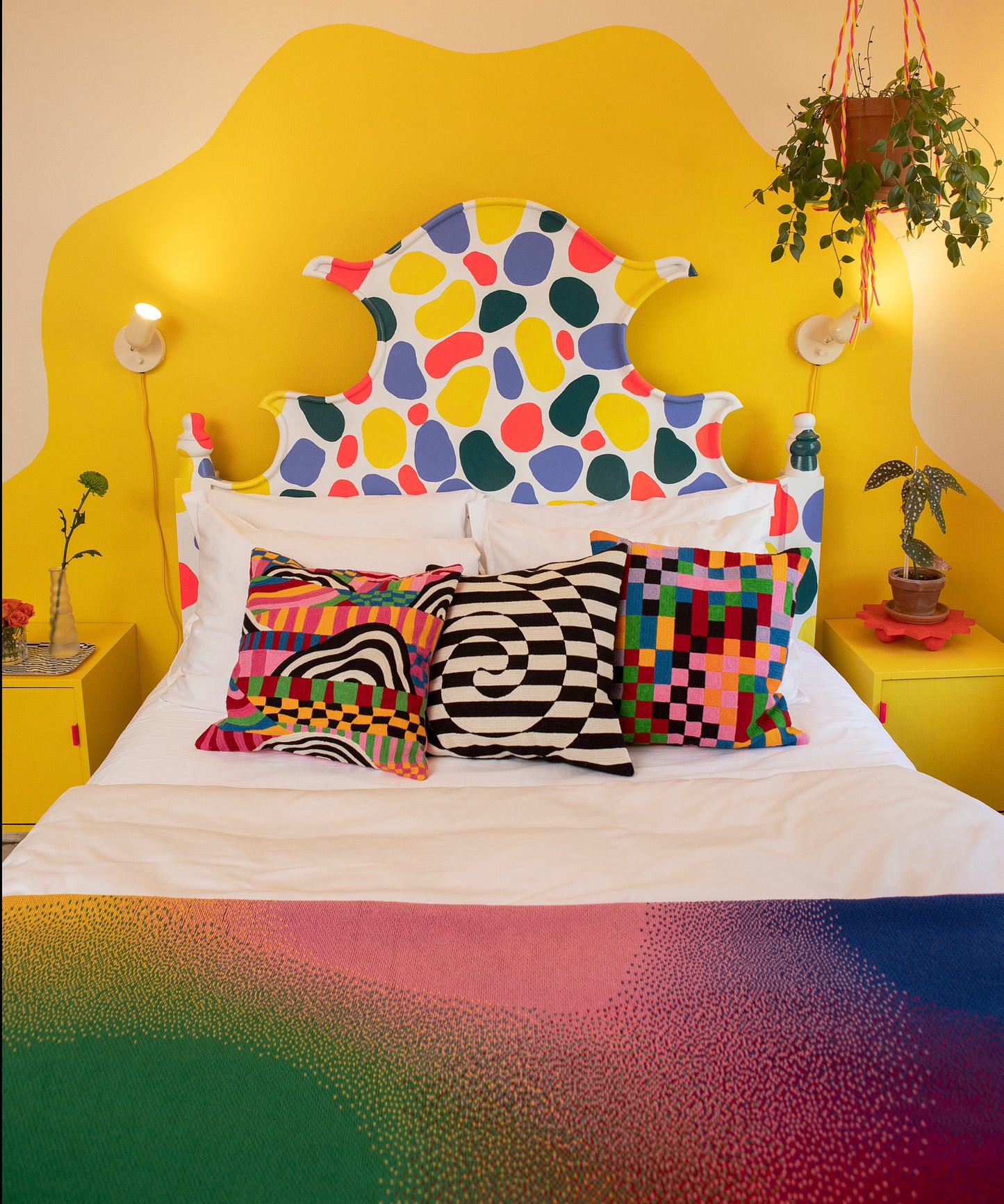 Image of a made bed in colorful bedroom. Aura blanket is shown on the mattress, topped with the Peaks & Valleys, Dazzle and Pixels Pillow Covers. 